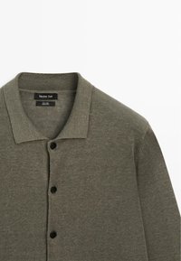 Chemise verte à manches longues, boutonnée avec col, trois boutons noirs visibles et étiquette "Massimo Dutti" à l'intérieur de l'encolure.