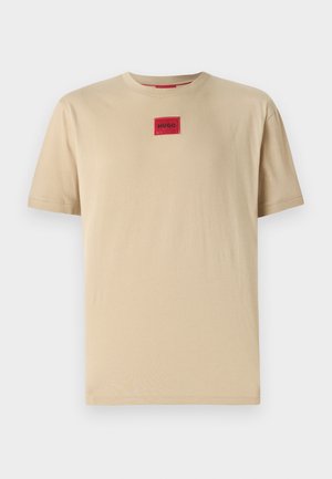 Beige cotton T-shirt with a relaxed fit, featuring a small red "HUGO" logo patch at the center and a classic crew neckline.