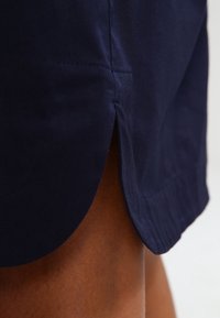 Mörkblå tygkjol med en lätt A-linjeform, som har sidofickor och synlig sömnadsdetalj. Slät textur, fållade kanter.