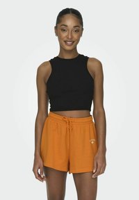 Zwarte geribde mouwloze crop top, gecombineerd met oranje shorts met trekkoord. De shorts hebben een klein wit logo aan de voorkant en een relaxed fit.