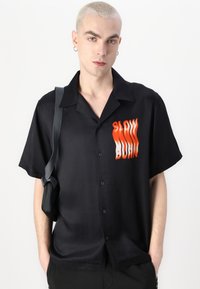 Zwart kortebloushirt met knopen in een gladde stof, uitgerust met een oranje "SLOW BURN" grafiek, heeft een ontspannen pasvorm en een zak.