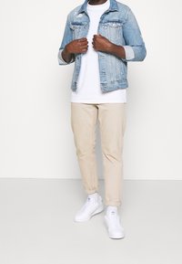 Světle modrá džínová bunda s opotřebovaným vzhledem, bílé tričko, béžové kalhoty se zúženými nohavicemi a bílé tenisky. Jednoduchý design s minimálním množstvím kovových doplňků.