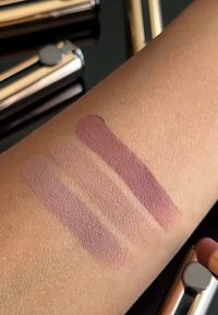 Tre matte leppestiftprøver i varierende nyanser av mauve er påført en lysebrune hudtone. Teksturen ser jevn og fløyelsmyk ut.