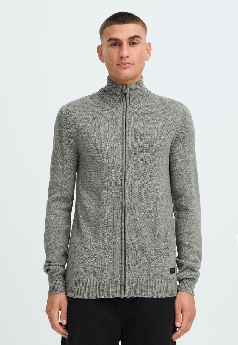 Grå hettejakke med høyt krage og lange ermer. Ribbete tekstur, tettsittende design og subtil merkevaretag på kanten.