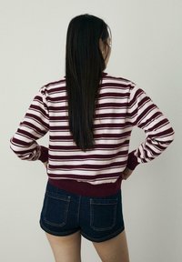 Marońsko-różowy sweter w paski z prążkowanymi mankietami i dolną częścią, w połączeniu z ciemnoniebieskimi szortami dżinsowymi z tylnymi kieszeniami.