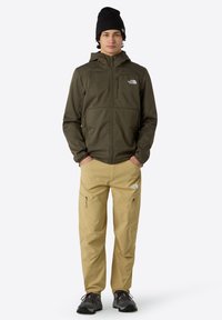 Zielona oliwkowa kurtka zapinana na zamek z kapturem; khaki spodnie cargo z zamkami; czarna czapka beanie. Teksturowana tkanina, funkcjonalny design, luźny krój.