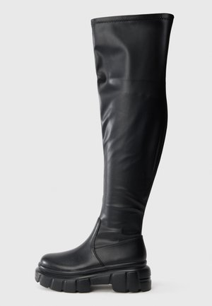 Čierne čižmy po kolená vyrobené z hladkej syntetickej kože. Hrubá, masívna gumová platforma so zaoblenou špičkou a dizajnom na obúvanie.