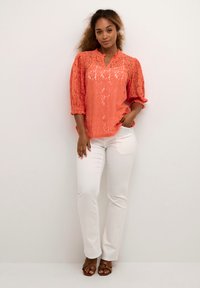 Coral lace blouse with a v-neck and three-quarter puff sleeves, paired with white straight-leg jeans and brown strappy sandals.