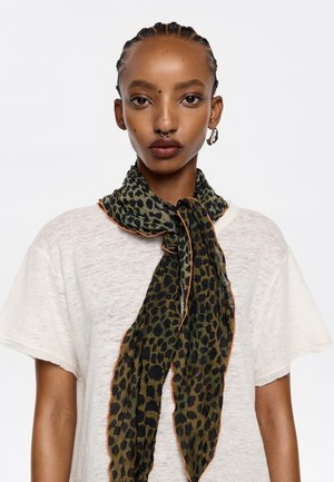 Foulard en soie présentant un motif léopard vert et noir, noué autour du cou avec un bord orange contrastant. Tissu léger et texturé.