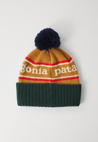Gorro de inverno em malha amarelo mostarda e verde escuro com pompom azul marinho e riscas vermelhas e brancas, apresentando texto branco parcialmente visível.