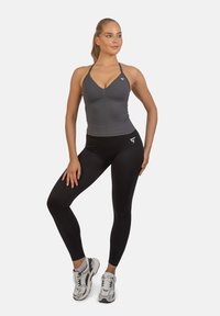 Grijze sporttop met halterbandjes en aansluitend design, gecombineerd met zwarte hoge taille leggings. Model draagt grijze en witte sneakers.