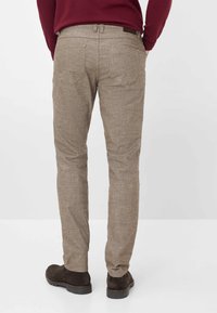 Beige Hosen aus strukturiertem Stoff mit geradem Bein, zwei Gesäßtaschen und einem braunen Taillenakzent. Getragen mit dunklen Stiefeln.