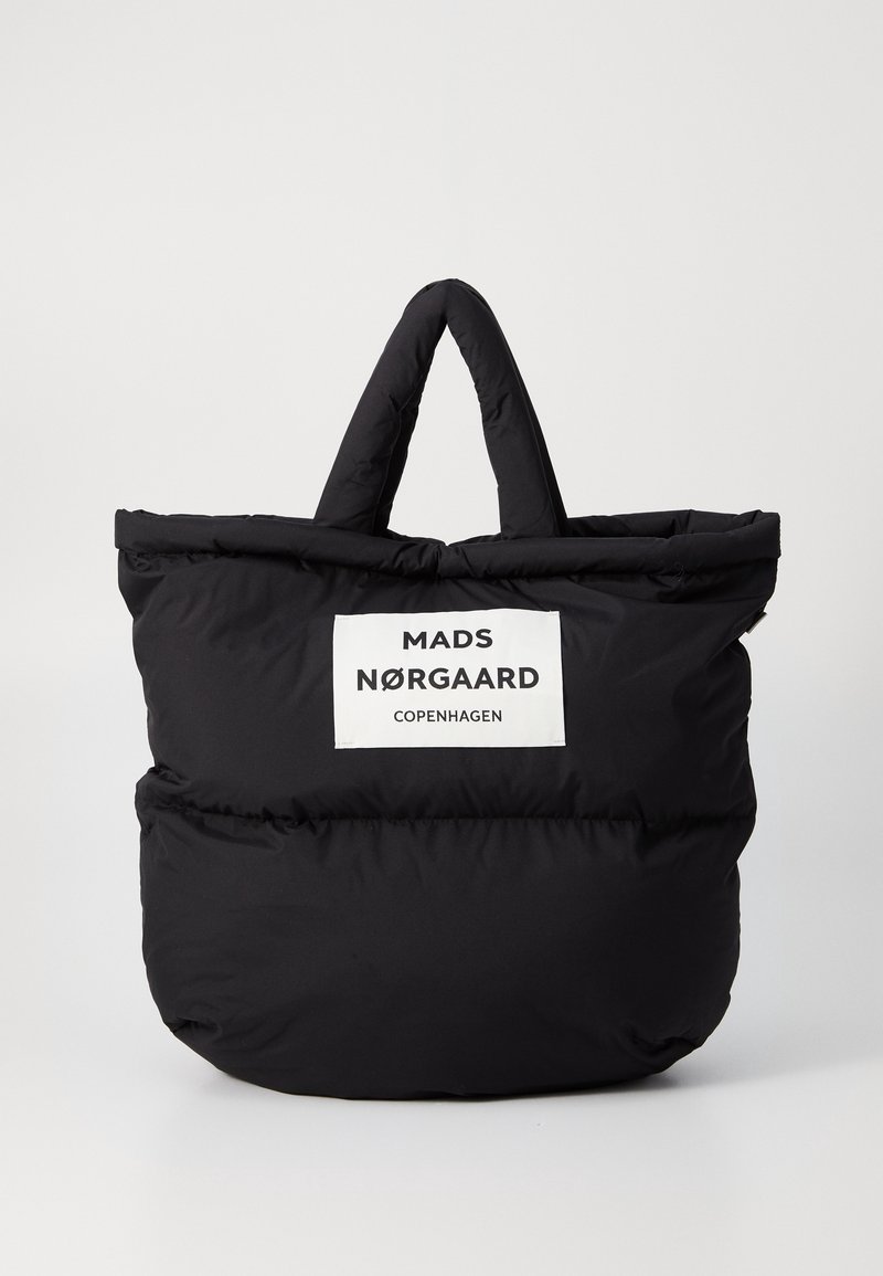 Czarna pufowa torba na ramię z podwójnymi uchwytami, z białą metką zawierającą napis "MADS NØRGAARD COPENHAGEN". Gładka, pikowana struktura.