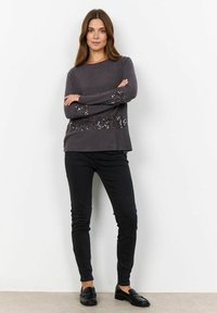 Grijze lange mouw sweater met pailletten over de borst en mouwen, gecombineerd met zwarte slim-fit broek en instappers.