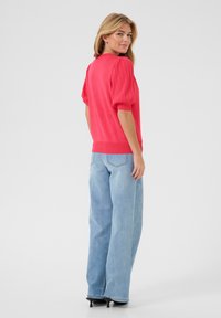 Pull rouge avec des manches bouffantes, texture côtelée et couleur unie, associé à un jean large bleu clair et des chaussures à talons noires.