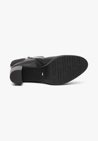 Black leather heeled shoe with a textured rubber outsole, side zipper, and a low block heel. Features subtle Italian flag accent.