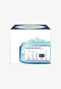 Clear glass jar with light blue cream and a blue and green lid, labeled with routine steps and product illustrations on the box.