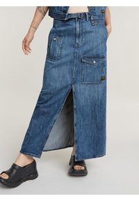 Denim maxi szoknya elöl hasítékkal, két oldalsó zsebbel és egy hátsó zsebbel. Az anyag közepes kék mosású, laza szabású.