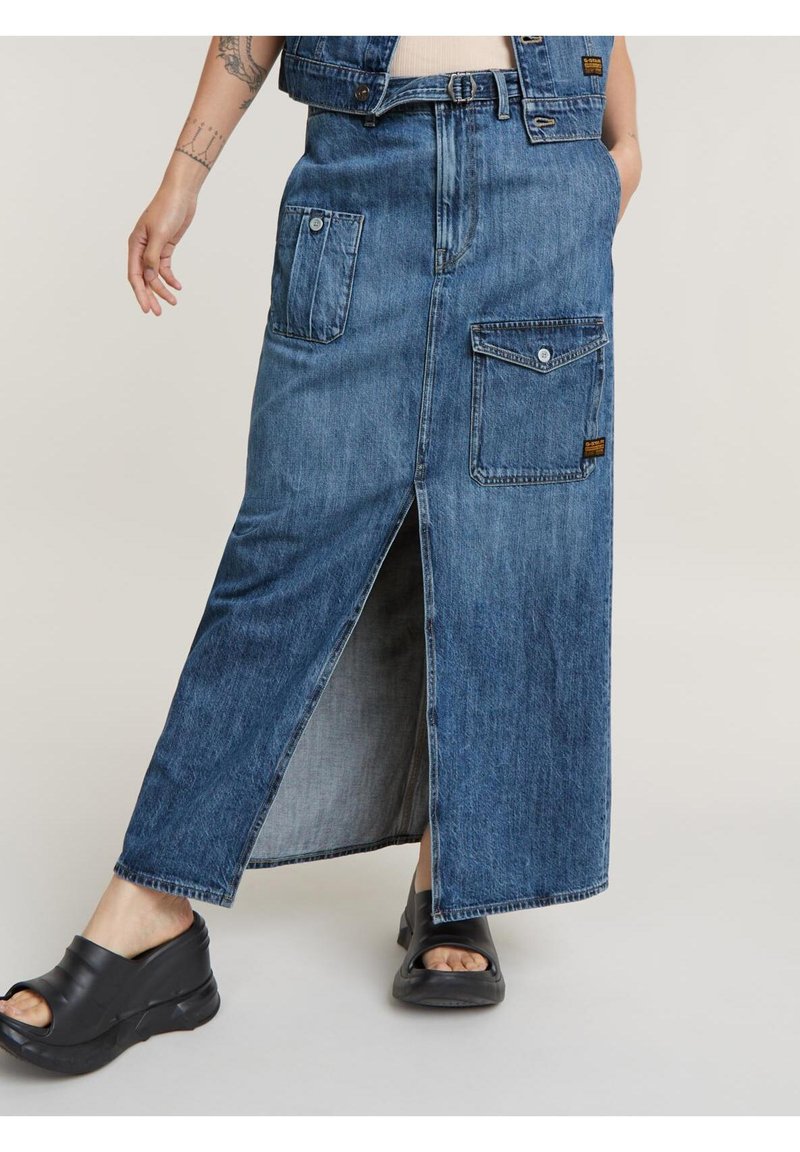 Denim maxi szoknya elöl hasítékkal, két oldalsó zsebbel és egy hátsó zsebbel. Az anyag közepes kék mosású, laza szabású.