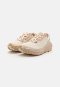 Scarpe da corsa beige con tomaia in mesh testurizzato, lacci piatti e suola ammortizzata. Presentano un logo discreto e stabilità del tallone rinforzata.