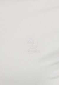 Tessuto bianco con texture e leggera elasticità, dotato di un piccolo logo ricamato al centro. Design liscio e minimalista, senza motivi.