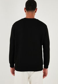 Sudadera negra con cuello redondo, mangas largas y puños acanalados. Tejido suave de color sólido, sin patrones ni adornos visibles.