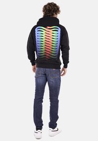 Felpa nera con un motivo a righe sfumate in blu, verde e rosso sul retro. Abbinata a jeans blu scuro e sneakers bianche.