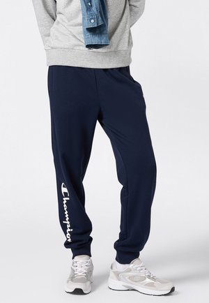 Pantaloni della tuta blu navy realizzati in tessuto morbido, con design affusolato e cintura elastica, con logo bianco "Champion" lungo la gamba sinistra.