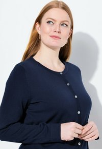 Námořnický svetr vyrobený z žebrované pleteniny, s kulatým výstřihem, zapínáním na pět knoflíků a dlouhými rukávy. Hladká textura, přiléhavý střih.