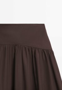 Jupe marron longueur genou avec une ceinture lisse et ajustée, texture froncée, réalisée en tissu léger, mettant en valeur de doux plis.