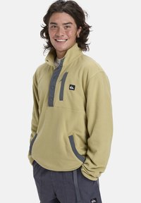 Fleece pullover in pale geel met grijze voorpaneel, knopen en zakaccenten. Heeft een hoge kraag en zijzakken.