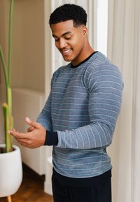 Sweatshirt rayé bleu et gris avec des manches longues, des poignets noirs et un col rond. Texture douce, design ajusté avec des accents de couleur subtils.