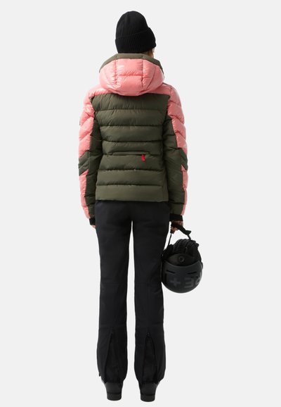 Gesteppten Jacke mit olivgrünem Körper und hellrosa Schultern, Kapuze und Akzenten. Schwarze Skihosen mit Reißverschlüssen an den Knöcheln.