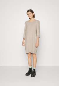 Abito in maglia beige lungo fino al ginocchio, con maniche a tre quarti, scollo rotondo e vestibilità rilassata; abbinato a stivali neri alla caviglia e calzini verde menta.