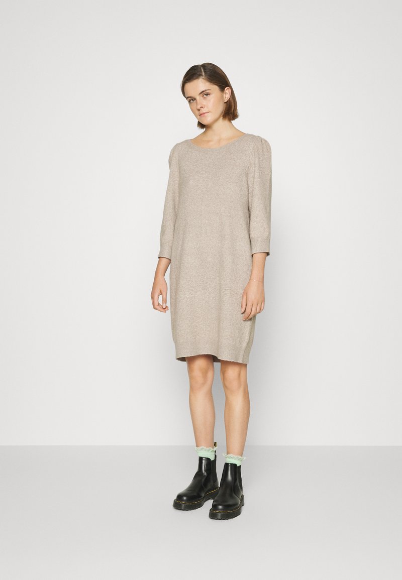Abito in maglia beige lungo fino al ginocchio, con maniche a tre quarti, scollo rotondo e vestibilità rilassata; abbinato a stivali neri alla caviglia e calzini verde menta.