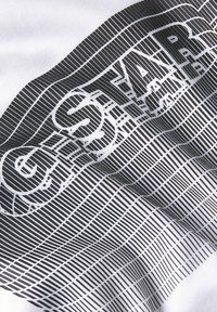 Tela blanca con un diseño gráfico negro que presenta líneas gruesas y la palabra "ESTRELLA" integrada en una serie de rayas verticales y horizontales.