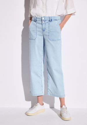 Světle modré volné džíny mají dvě přední kapsy a zapínání na knoflík. Materiál vypadá jako měkký denim, s jemnými švy a uvolněným střihem.