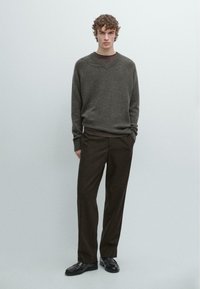 Szary dzianinowy sweter z dekoltem w serek, noszony na brązowej koszuli. Do kompletu brązowe spodnie i czarne sznurowane buty.