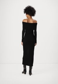 Svart off-shoulder ribbad stickad klänning med långa ärmar, figurnära silhuett och knälång längd, i kombination med svarta klackstövlar.