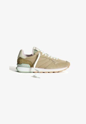 Sneaker de sport beige avec des matériaux en daim et en maille, lacets blancs, accents verts sur le talon et semelle en caoutchouc texturée. Présente le logo "HOFF".