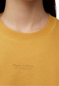 Sudadera de algodón amarilla con cuello acanalado y logo impreso en un tono contrastante. Textura suave con un ajuste casual.