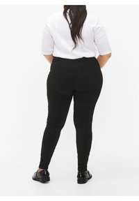 Czarne legginsy o gładkiej teksturze i dopasowanym kroju, z wysokim stanem i minimalnymi szwami, w zestawieniu z białą bluzką z prążkowanego materiału.