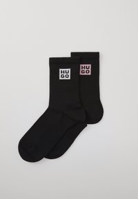 Calze nere con texture a coste, dotate di loghi quadrati bianchi e rosa con la scritta "HUGO" sul lato. Design di lunghezza media fino al polpaccio.