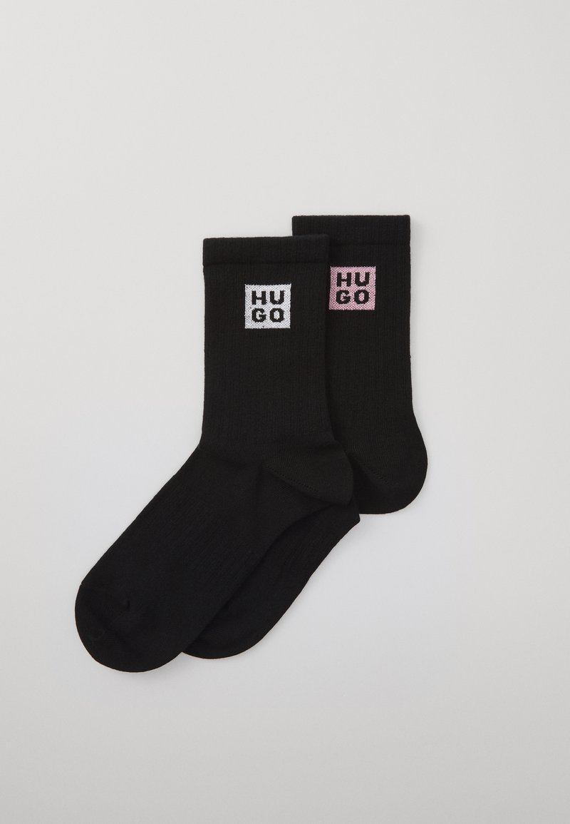 Calze nere con texture a coste, dotate di loghi quadrati bianchi e rosa con la scritta "HUGO" sul lato. Design di lunghezza media fino al polpaccio.