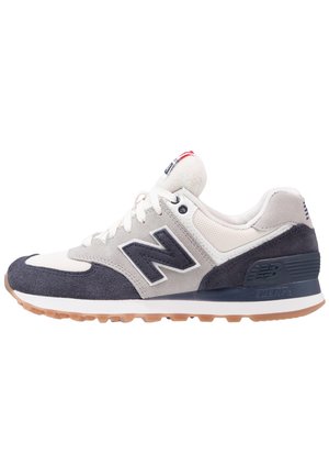 Men's gray and navy New Balance sneaker with suede and mesh panels, white laces, and gum rubber sole, side view against white background.