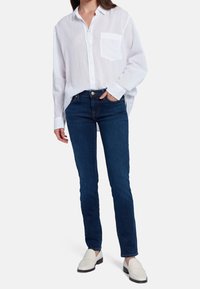 Camisa blanca de botones con un bolsillo en el pecho, combinada con Jeans slim-fit de color azul oscuro y mocasines de color claro. Tela suave y diseño clásico.