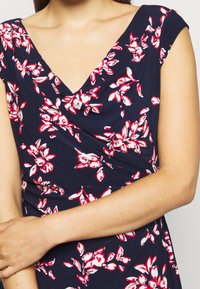 Marinblå klänning med vit och röd blommönster, V-ringning, korta ärmar och samlad tygdetalj över framsidan. Mjuk, elastisk material.