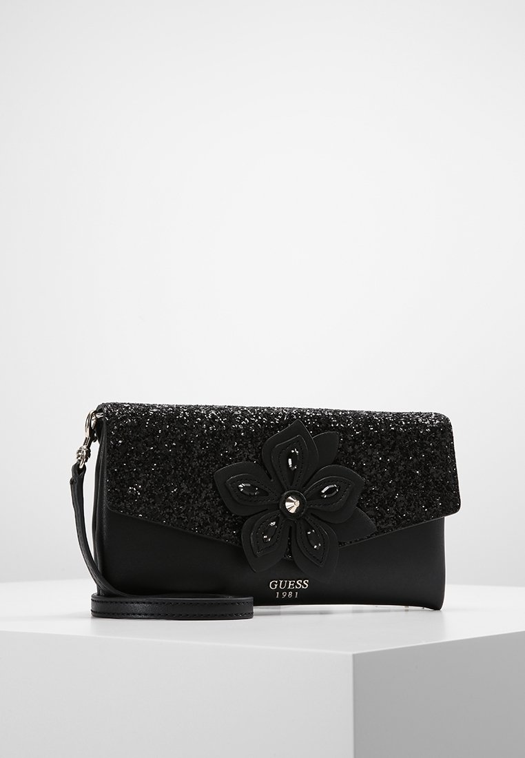 Sac à main noir avec un rabat pailleté noir, orné d'un grand accent floral. Texture lisse, bandoulière détachable et logo de marque métallique.