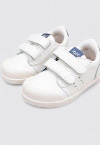 Zapatillas blancas para niños con dos correas de velcro, suela de goma texturizada y sutiles acentos azules, que presentan detalles perforados en los lados.