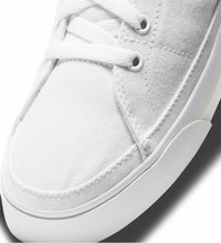 White canvas sneaker with textured upper, round toe, and white rubber sole. Features white laces and eyelets, with visible stitching details.